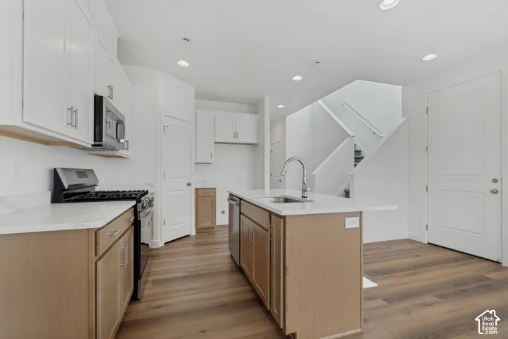 White upper cabinetry, light wood-finish lower cabinetry, a stainless steel range, and a kitchen island with an integrated sink and dishwasher