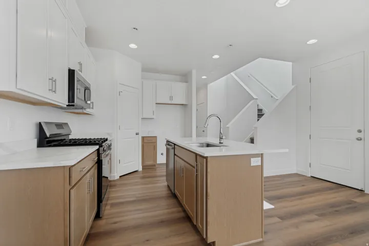 White upper cabinetry, light wood-finish lower cabinetry, a stainless steel range, and a kitchen island with an integrated sink and dishwasher