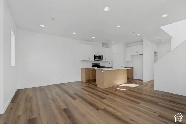 Open-concept living space with wood-finish flooring, recessed lighting, white cabinetry, and stainless steel appliances