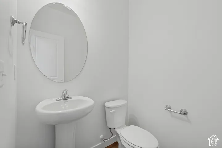 Pedestal sink with chrome faucet, oval frameless mirror, and white toilet