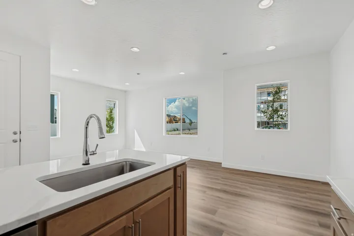 Kitchen island with a stainless steel undermount sink, gooseneck faucet, light-toned countertop, and wood-finish cabinetry