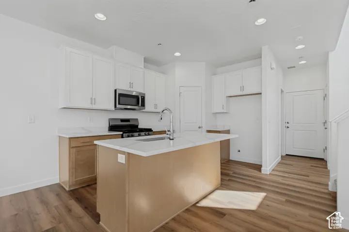 Kitchen featuring white upper cabinetry, light wood-finish lower cabinetry, a center island with a white countertop, stainless steel appliances, and wood-finish flooring