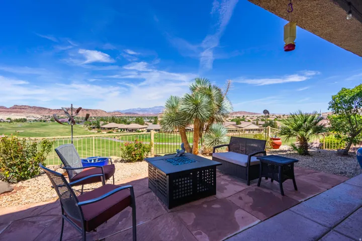 Expansive covered patio with stamped concrete flooring, featuring a built-in fire pit with seating, mature palm trees, and manicured landscaping