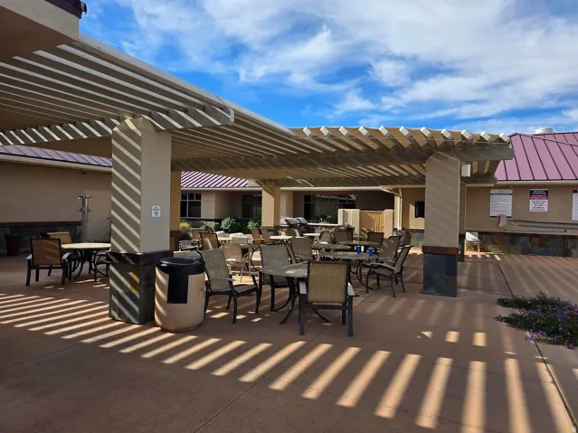 Covered outdoor lounge area with slat pergola, stone-clad pillars, and integrated hardscaping