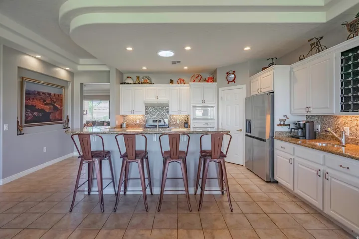 Kitchen featuring white cabinetry, a built-in microwave, a stainless steel refrigerator, and granite countertops with a tile backsplash