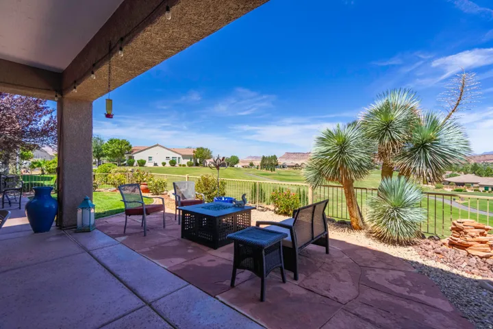 Covered patio with integrated lighting, extending to a custom flagstone patio, surrounded by desert landscaping and an iron fence