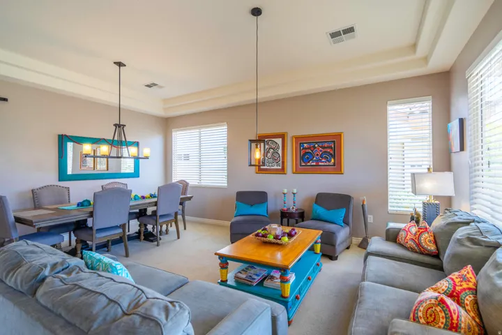 Spacious open-concept formal living and dining area featuring light carpet, coffered ceiling with recessed lighting, and multiple windows with plantation shutters providing natural light