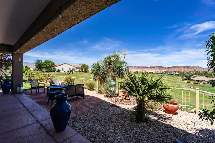 Covered patio with concrete flooring overlooking expansive manicured lawn, mature palm trees, and desert landscaping with native plantings