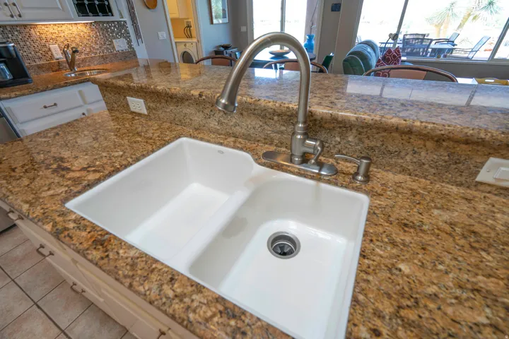 Granite countertop kitchen island featuring a dual-basin white composite sink with an arched stainless steel faucet and matching soap dispenser
