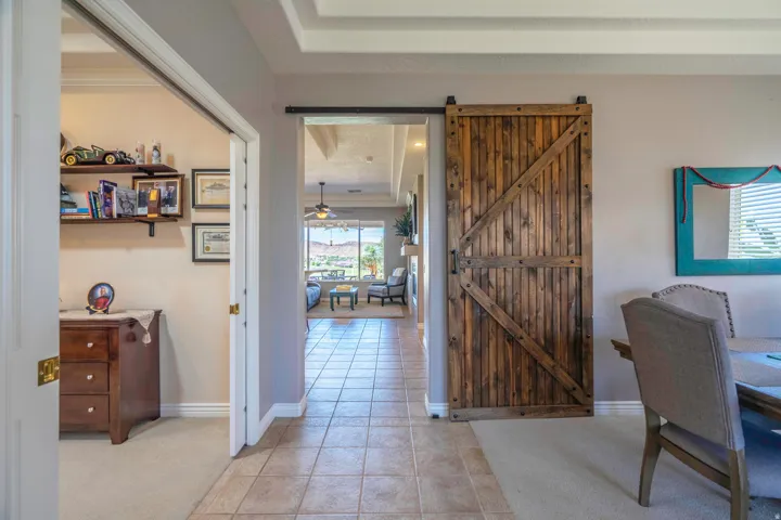 Spacious hallway featuring tile flooring, architectural barn door with sliding hardware, built-in shelving and cabinetry, coffered ceiling detail, and abundant natural light from multiple windows