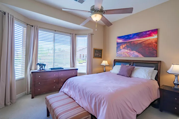 Bright 2nd bedroom with triple bay windows, ceiling fan with integrated lighting, wood-finish dresser with drawer storage, and artwork accent wall