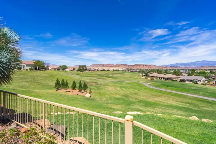 Expansive green landscape with a golf course, distant red rock formations, and residential properties