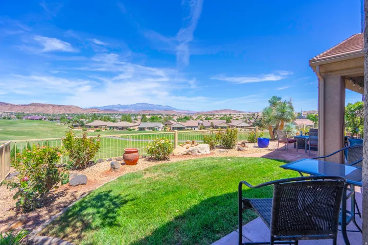 Expansive backyard oasis featuring manicured lawn, mature landscaping with established shrubs and trees, and a covered patio with column supports