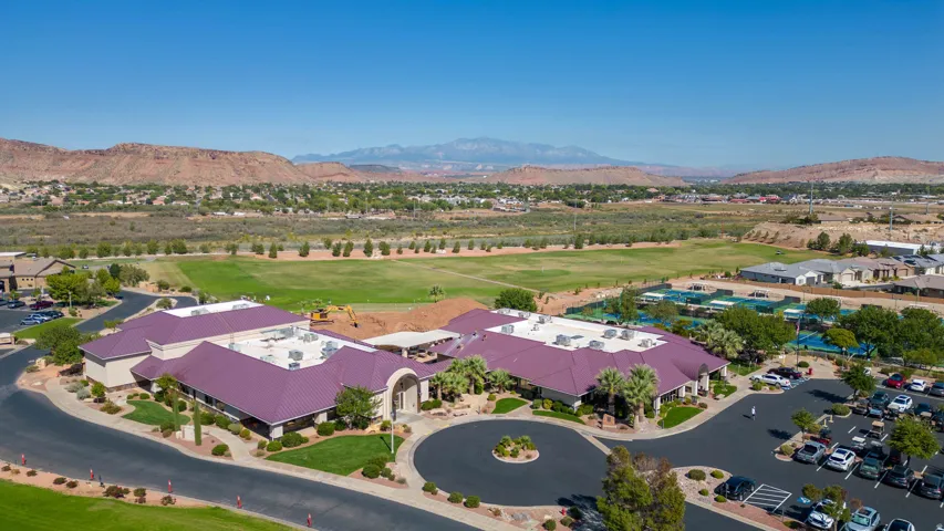 Expansive community complex with a circular drive, abundant parking, a manicured green space, and tennis courts, set against a mountainous backdrop