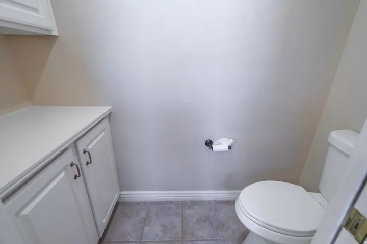 White cabinetry with bronze hardware, white countertop, white toilet, and gray tile flooring