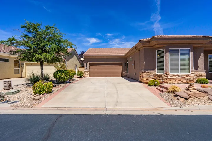 Stucco exterior with a stone veneer accent, attached garage, long concrete driveway, and xeriscaped landscaping