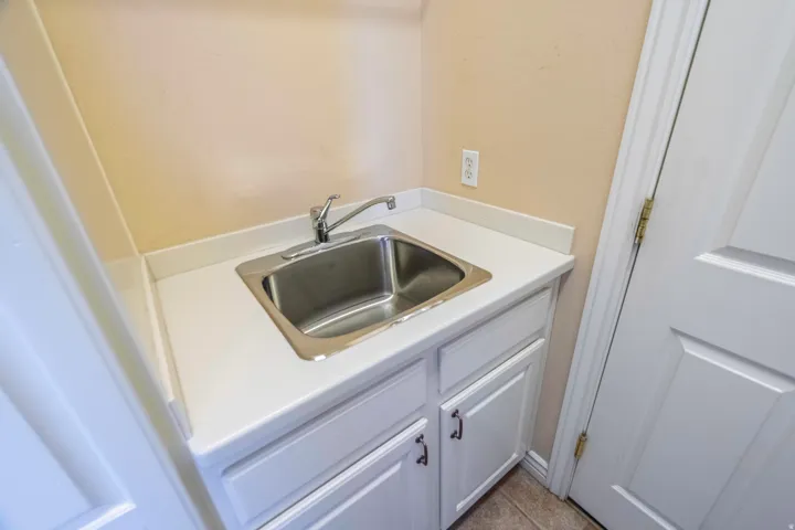 Compact kitchenette featuring a stainless steel drop-in sink with chrome faucet, white cabinetry with hardware pulls, laminate countertop, and ceramic tile flooring