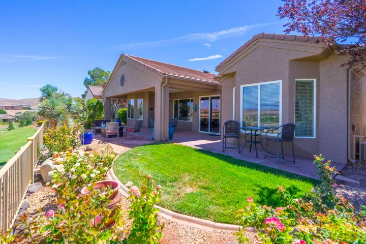 Expansive backyard featuring a manicured lawn, established landscaping, and a covered patio area with direct outdoor access
