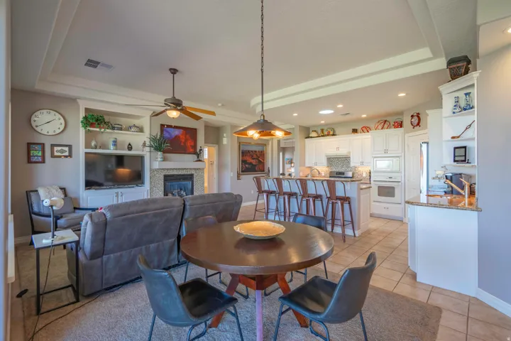 Family room  with tray ceiling with recessed lighting, built-in shelving, fireplace with tiled surround, wood-finish ceiling fan, and a kitchen island with bar seating