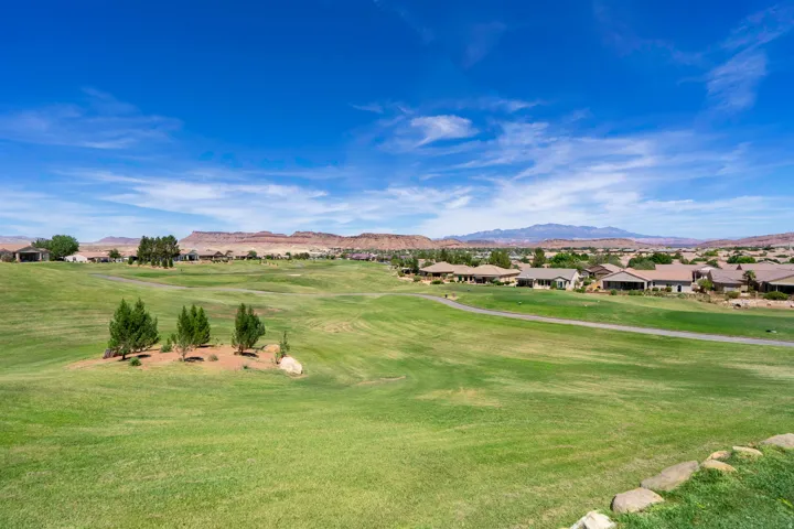Expansive green landscape (golf course) with distant residential properties, rugged mountains, and a clear blue sky