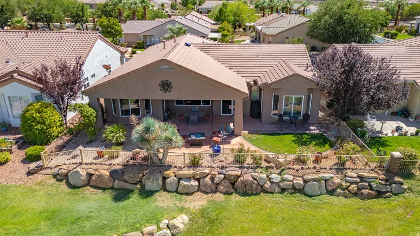 Rear exterior featuring a covered patio, tiled roofing, stucco siding, and a stone retaining wall