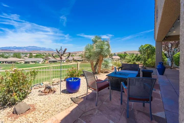 Paved patio with decorative rocks, mature desert plantings, and a white metal fence overlooking a golf course and distant mountains