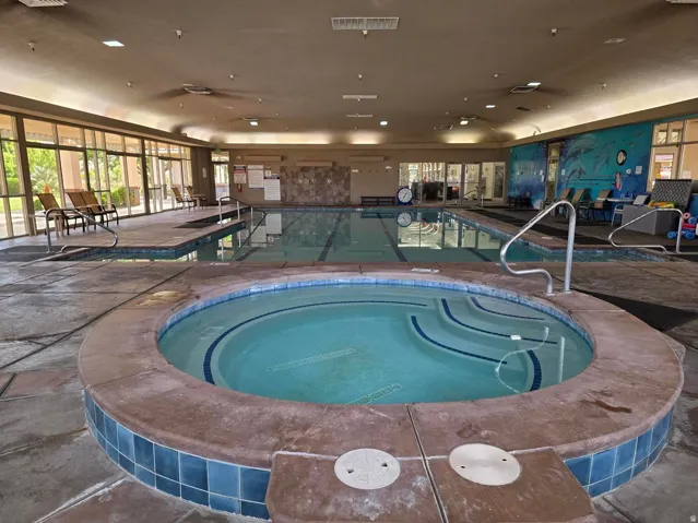 Indoor heated swimming pool with a distinct hot tub, surrounded by a stone-look deck