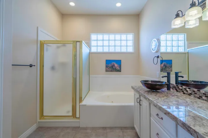 White vanity with stone-finish countertop, dual vessel sinks with wall-mounted faucets, and an enclosed shower with gold-finish framing