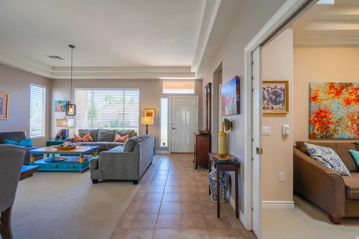 Open-concept living area featuring tile flooring, recessed ceiling details, and abundant natural light from multiple windows with plantation shutters