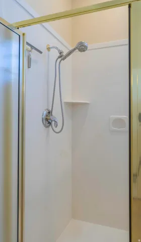 Modern shower enclosure featuring frameless glass panels with brushed nickel hardware, dual showerheads with handheld spray option, and a built-in recessed shelf for storage convenience