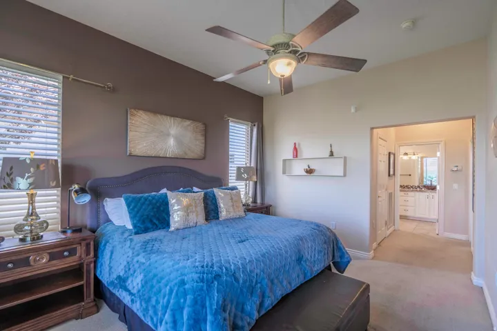 Vaulted ceiling with a ceiling fan, two windows with horizontal blinds, built-in wall shelf, and a bathroom with a white vanity and dual sinks