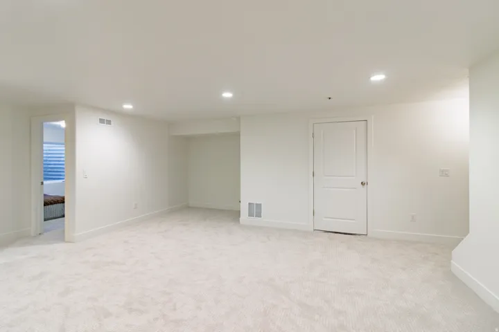 Spacious basement recreation room featuring neutral carpet flooring, recessed ceiling lighting, and multiple white painted doors