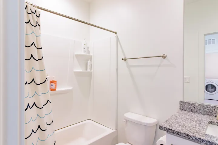 White bathtub and shower combination with integrated shelving, white toilet, and a vanity with a light-toned countertop