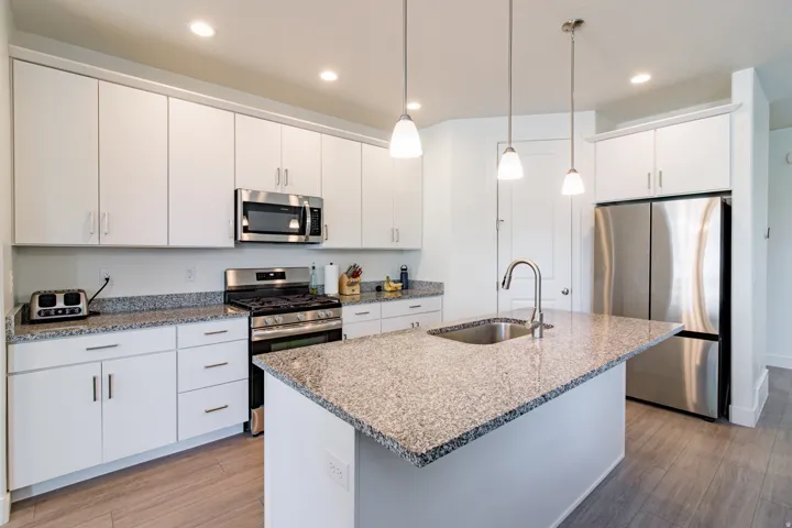 Kitchen featuring white cabinetry, stainless steel appliances, granite countertops, a kitchen island with an undermount sink, and wood-finish flooring