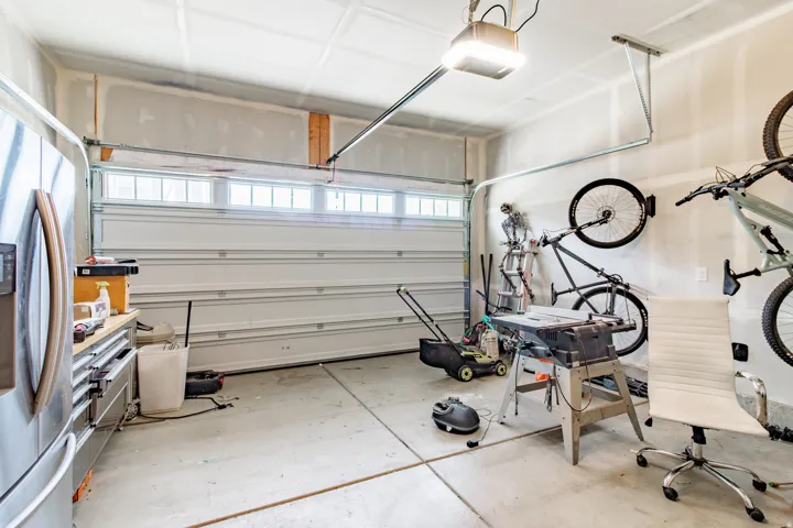 Attached garage with a sectional garage door featuring upper window panels, exposed ceiling joists, and a concrete floor