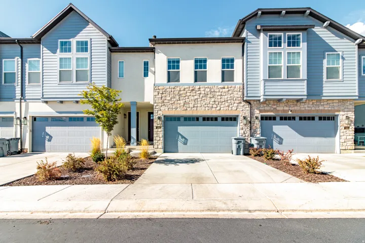 Modern townhome community featuring light-filled facades with extensive multi-pane windows, stone and siding exterior accents, and three-car garage doors with contemporary paneling