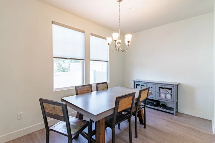 Recessed ceiling lighting, wood-finish flooring, two large windows, white roller shades, and a chandelier with glass shades