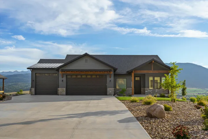 Ranch-style residence featuring a gray exterior with stone accents, a dark shingle roof, and an attached three-car garage