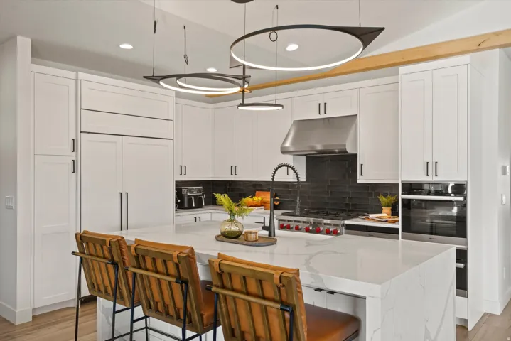 White shaker-style cabinetry with matte black hardware, integrated refrigerator, stainless steel range hood, built-in double oven, and a kitchen island with a light-toned countertop