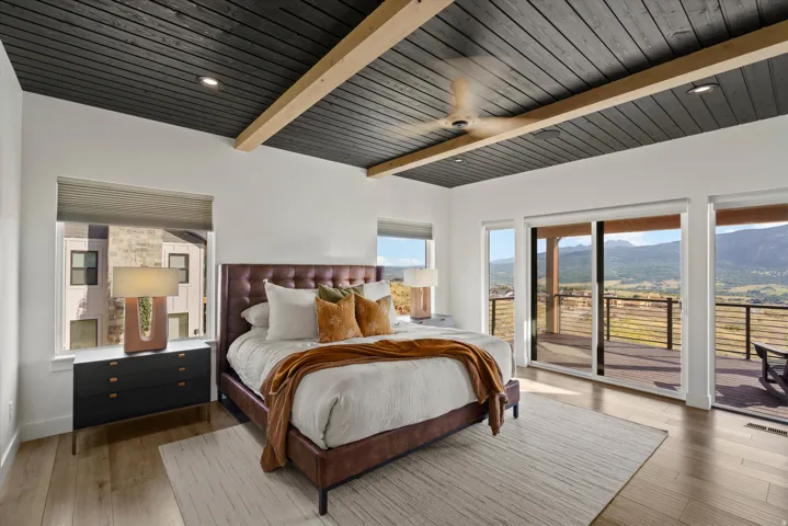 Tray ceiling with wood paneling and exposed beams, recessed lighting, wood-finish flooring, sliding glass doors to outdoor deck, mountain backdrop