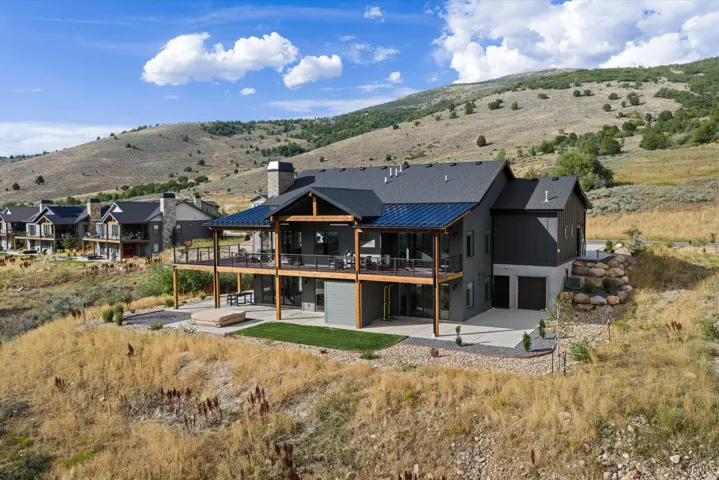 Multi-level home featuring an expansive upper deck and lower patio, dark gray siding, a stone-clad chimney, and an attached two-car garage