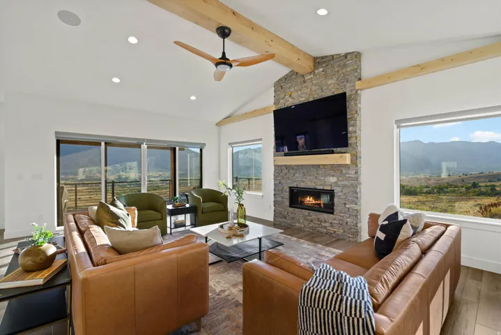 Vaulted ceiling with exposed wood beams, stone fireplace, integrated fireplace, recessed lighting, and large windows