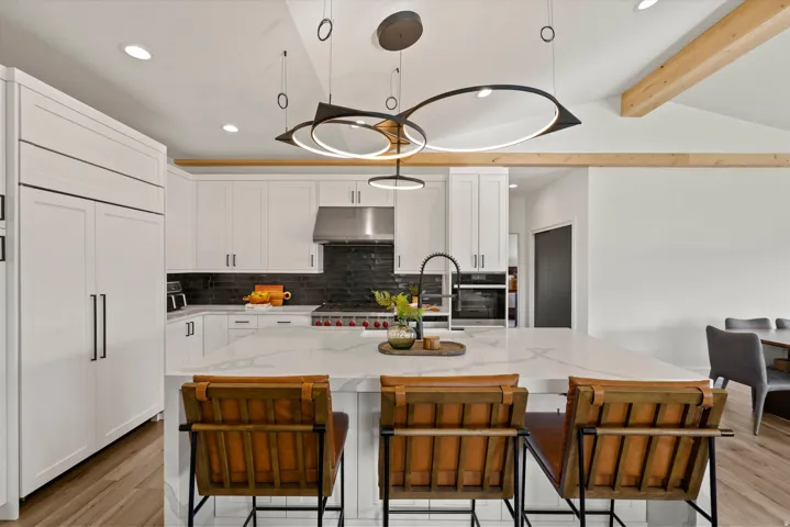 White cabinetry, stainless steel appliances, dark tile backsplash, a center island with countertop seating, and exposed wood ceiling beams
