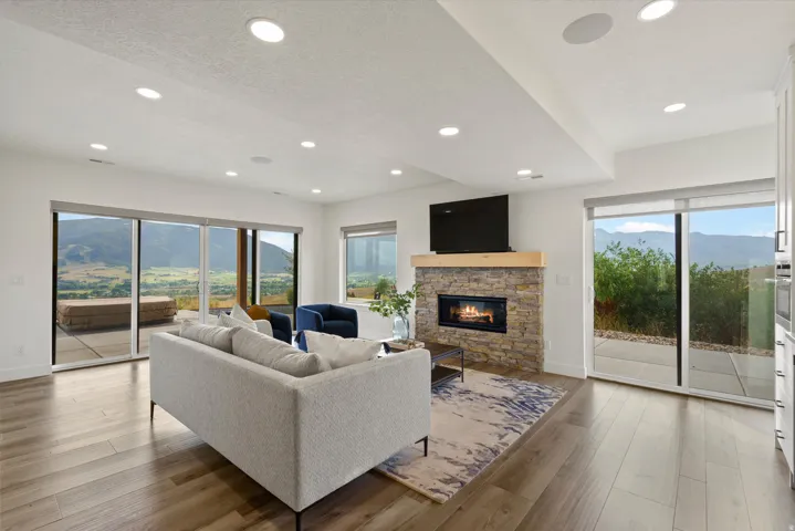 Expansive living area with wood-finish flooring, a stone fireplace with a wood mantle, and recessed lighting