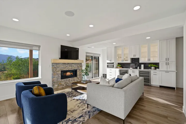 Recessed lighting, wood-finish flooring, stone-clad fireplace with a wood mantel, built-in cabinetry with glass-front uppers, and integrated beverage refrigerators