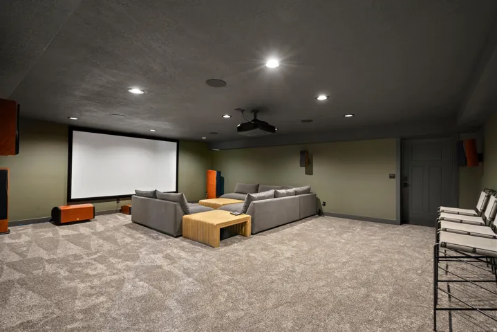 Expansive carpeted room featuring a large projection screen, recessed lighting, and a paneled interior door