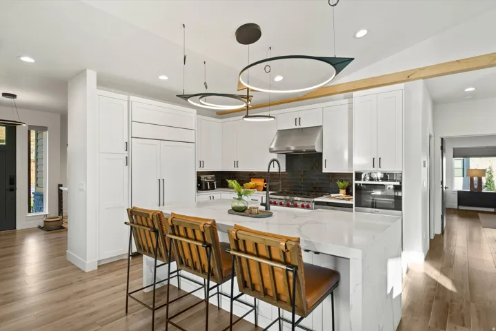 Modern kitchen featuring white shaker cabinetry, an expansive waterfall island, integrated stainless steel appliances, and wood-finish flooring