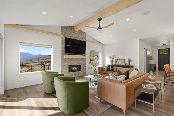 Vaulted ceilings with exposed beams, stone-faced fireplace, wood-finish flooring, recessed lighting, and a modern ceiling fan