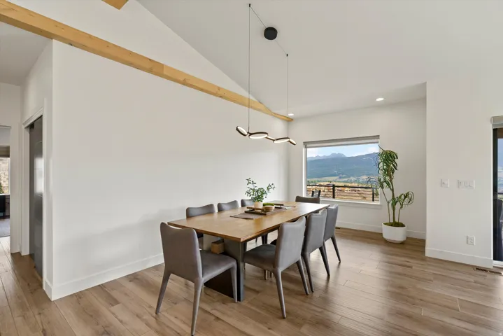 Vaulted ceiling with exposed wood beam, wood-finish flooring, and a modern linear chandelier