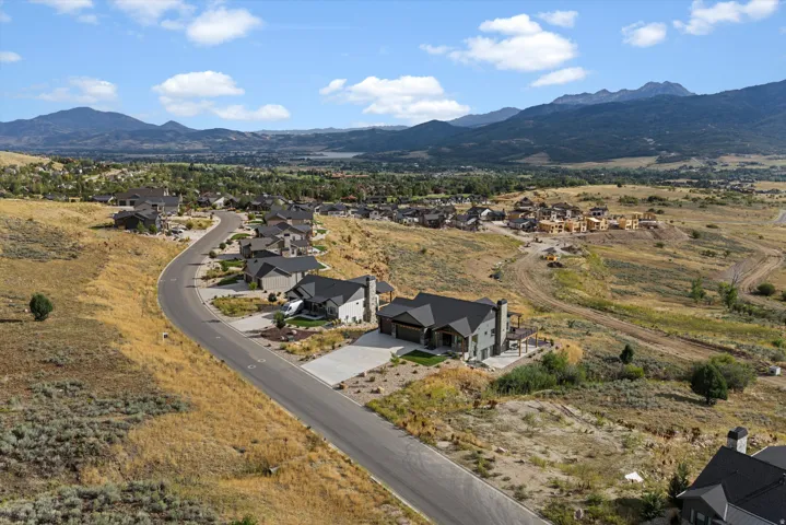 Curved residential street with modern homes, mountain backdrop, and distant body of water